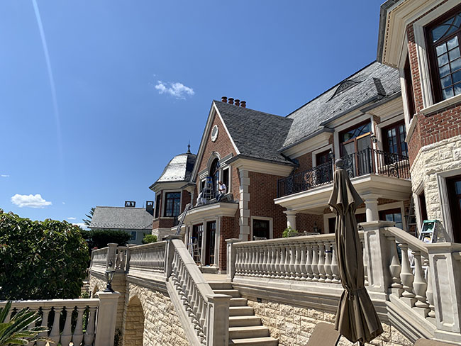 Elegant mansion with brick and stone exterior, featuring balconies, large windows, and a staircase leading to a landscaped courtyard.