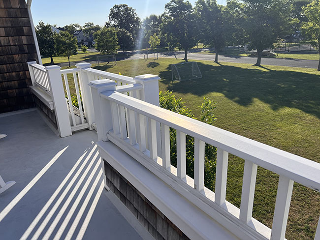 A sunlit balcony railing overlooks a grassy area with trees and playground equipment, casting long shadows on the floor.