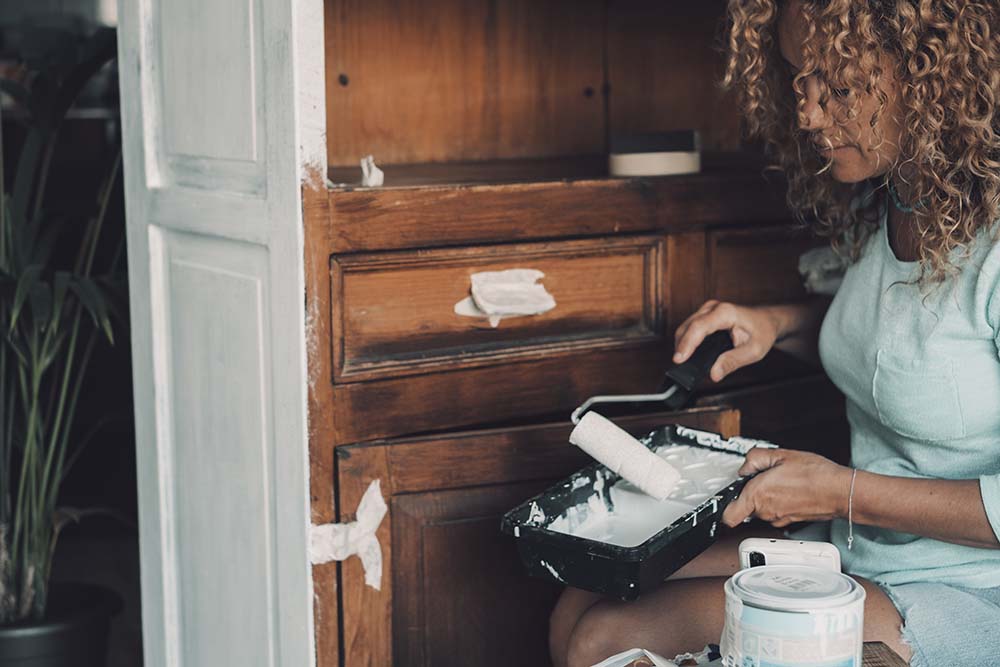 A woman restores her cabinet by painting it with a new color. 