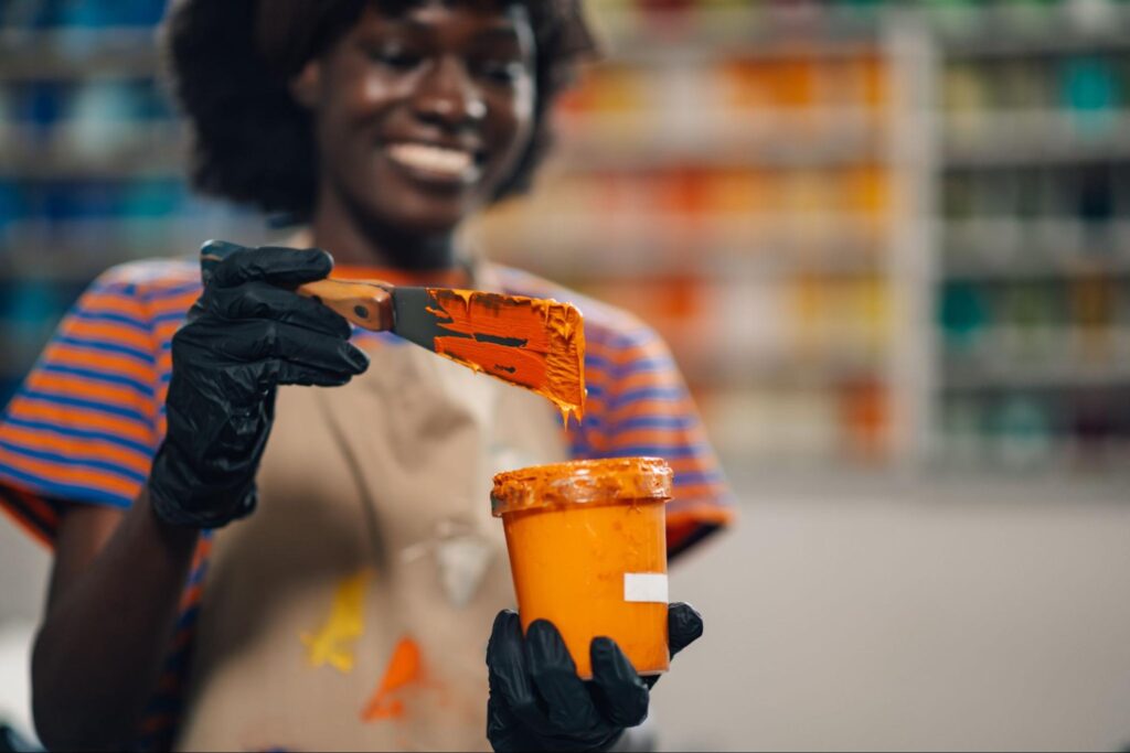 A woman is happily holding a small container of orange paint.