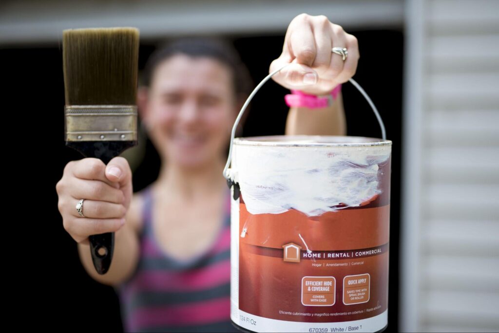 A woman is holding up a can of opened paint with a paintbrush.