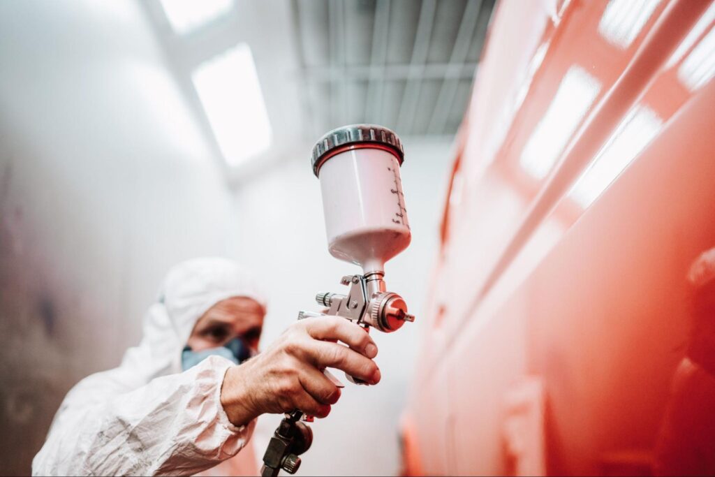 A close-up of a man in protective gear is spraying paint on a large object.