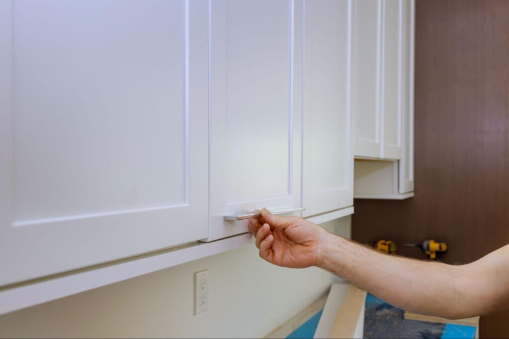 A close-up of someone grabbing the handle of a white cabinet.