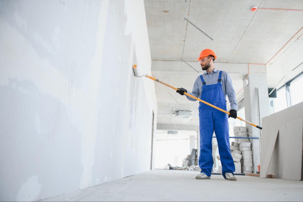 A contractor paints a commercial building wall with a roller.