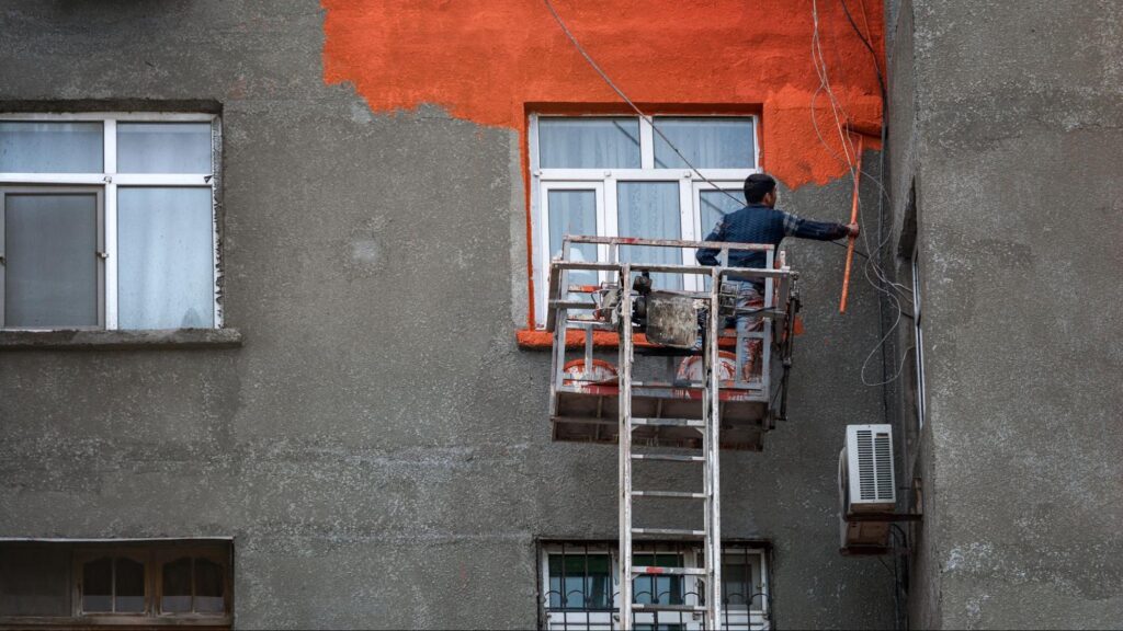 A worker painting the exterior walls of a residential building.