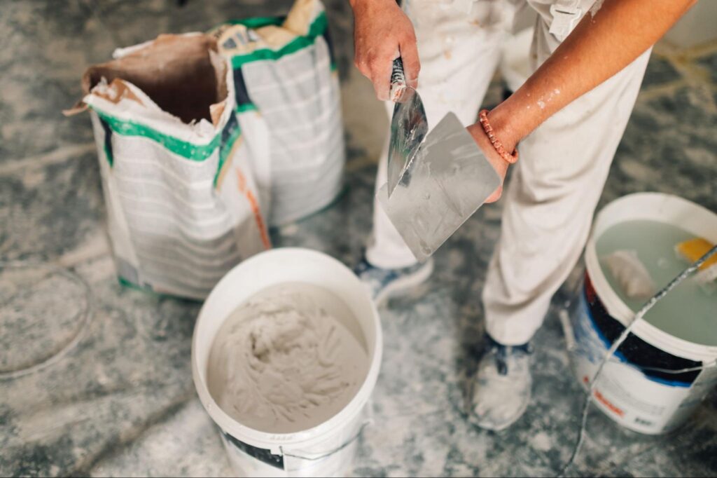A worker is standing over a bucket of spackle.