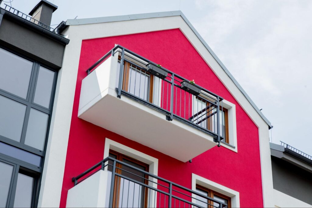 Freshly completed exterior home painting of a red house with white trim and a balcony.