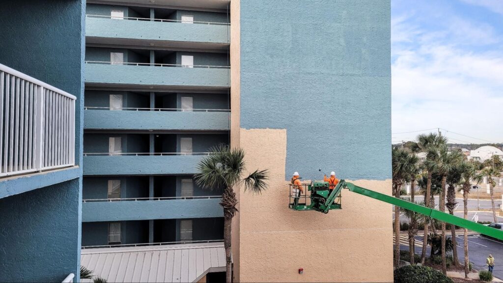 Crane lifts commercial painters to apply a new blue exterior coating.