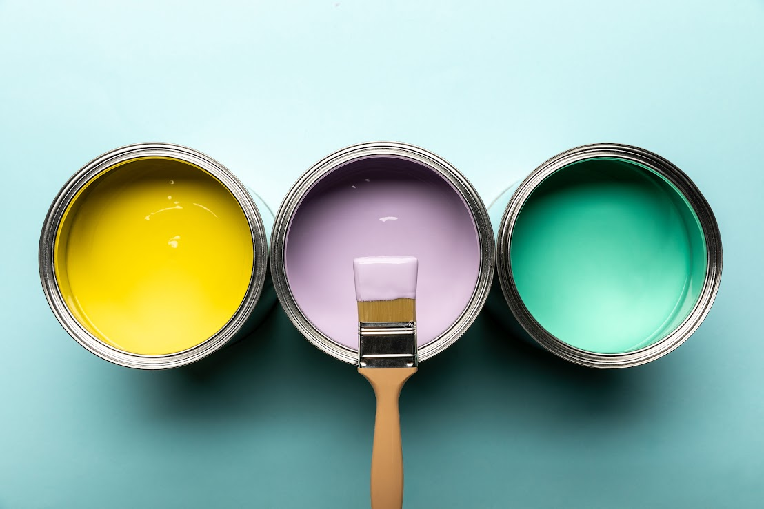 Three open paint cans in three different colors, with a paintbrush on top of the middle paint can, illustrating a concept for choosing the best paint for interior walls.