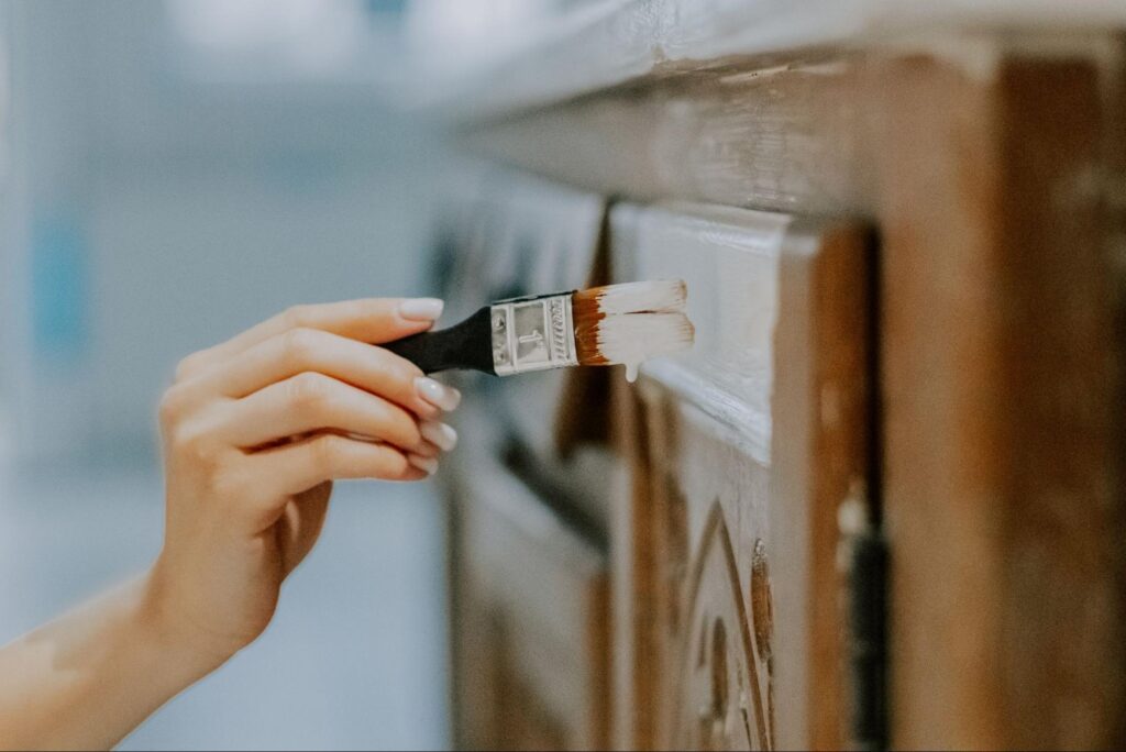A close look at someone painting a cabinet with a small paintbrush.