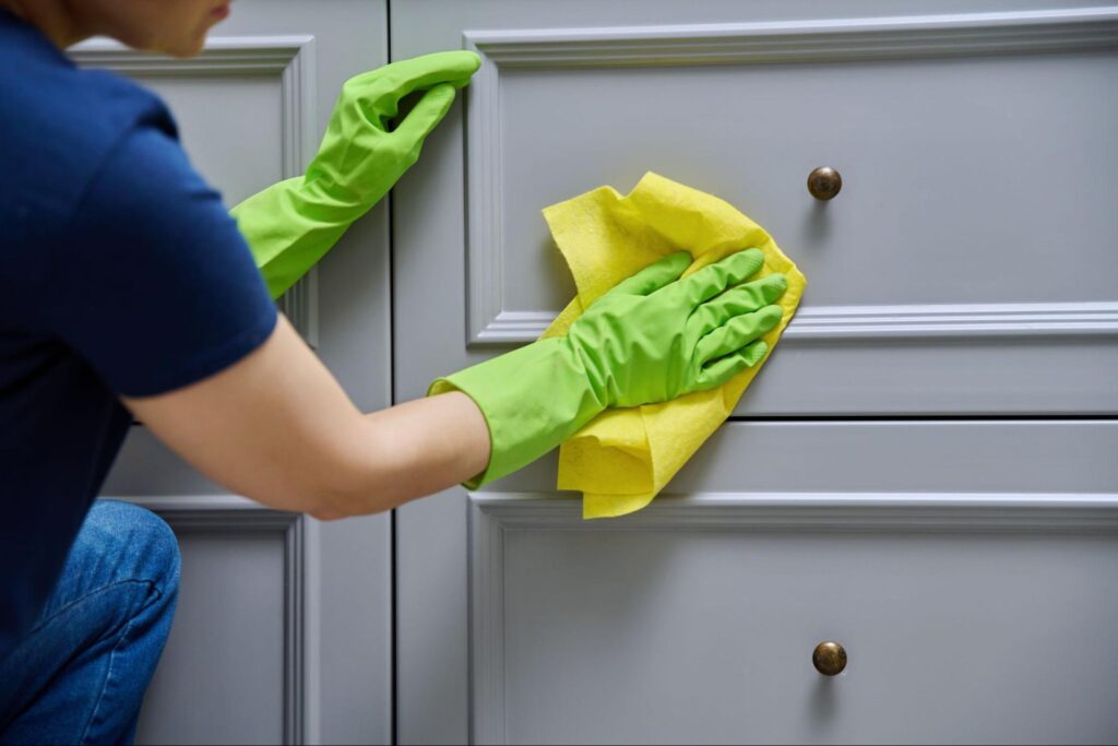 A woman cleans a freshly painted cabinet surface with a microfiber cloth.