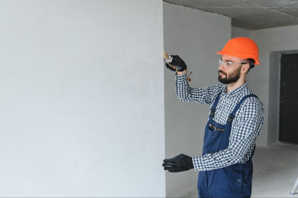 A professional residential painter applies a primer to an interior wood wall.