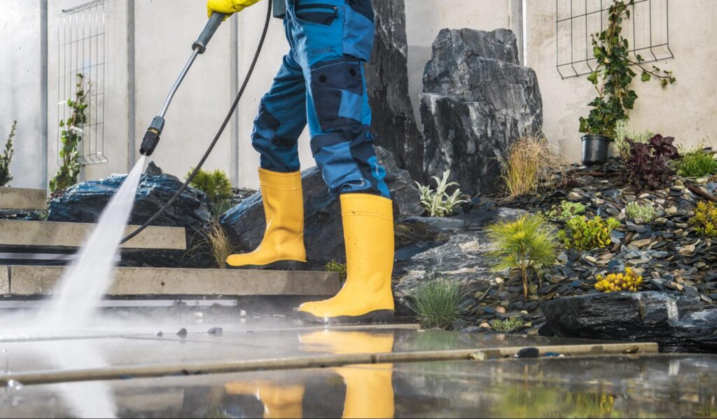 A gardener uses a power wash to remove the dirt on the tiles in the garden.
