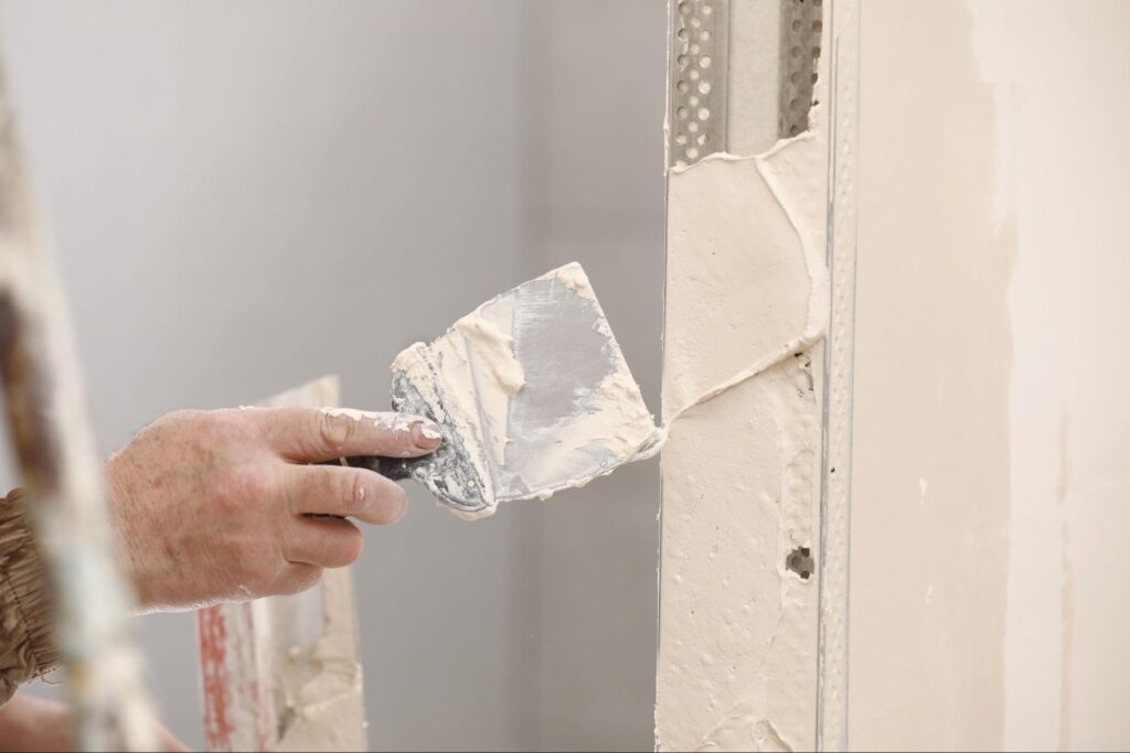 A worker is applying spackle to a wall.
