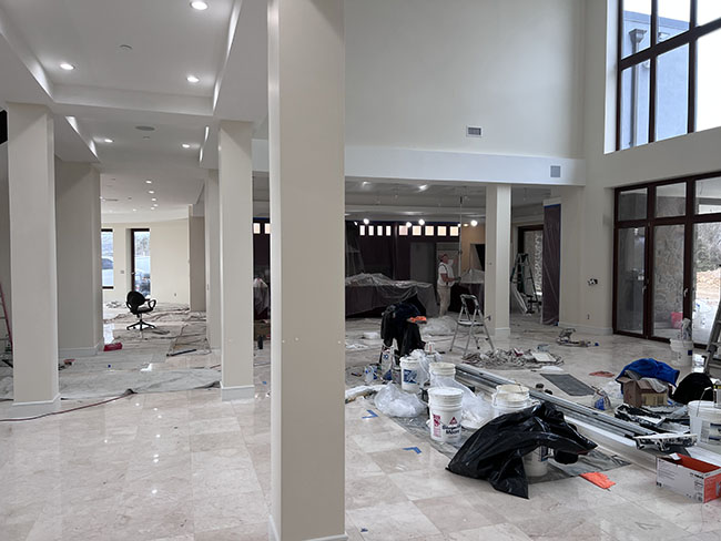 A spacious, unfinished room with marble floors, construction materials, and workers in the background, indicating a renovation in progress.