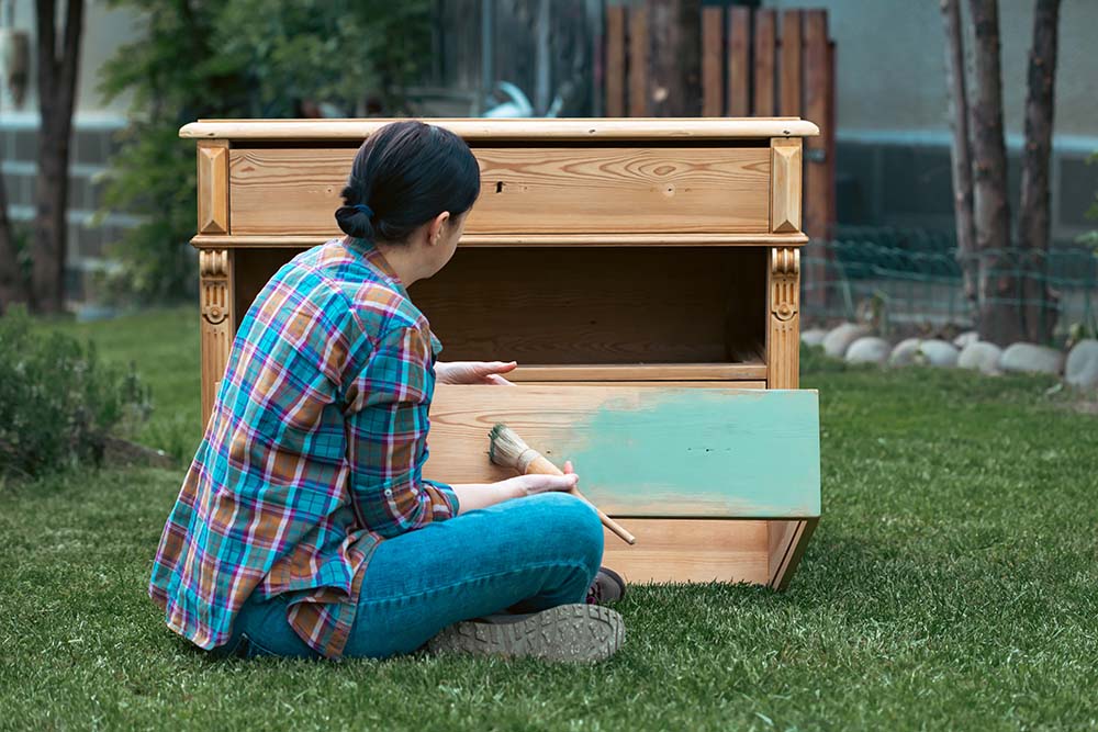 A young woman paints a cabinet outside her home. 